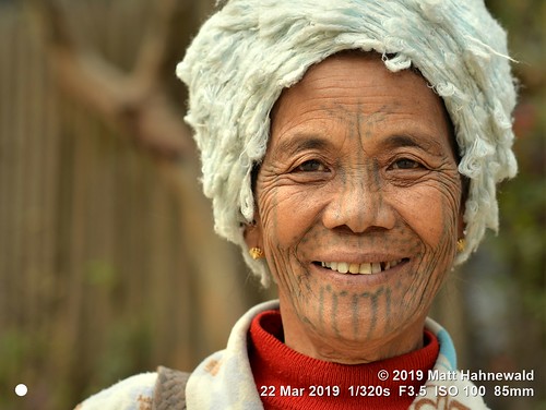 matthahnewaldphotography facingtheworld qualityphoto character head face forehead nose chin tribal tribe traditional tattoo facialtattoo eyes expression consensual conceptual diversity humanity living travel lifestyle tradition exotic ethnic hilltribe local rural cultural village mindat chinstate myanmar burma asia asian person one female old woman women detail nikond610 nikkorafs85mmf18g 85mm street portrait closeup headshot fullfaceview outdoor colour posing authentic smiling cap teeth muun elderly lookingatcamera