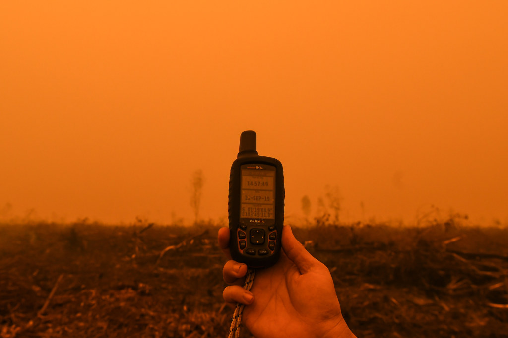 綠色和平組織走入林火災區，在濃濃的煙霾籠罩下，出示坐標定位設置。此地點位於蘇門答臘東部佔碑省的PT Wira Karya Sakti (WKS)種植園地。WKS 是印尼金光集團的子公司。攝於2019年9月21日， Muhammad Adimaja / Greenpeace