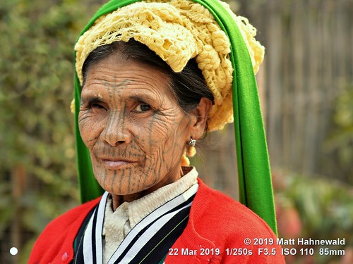 matthahnewaldphotography facingtheworld qualityphoto character head face forehead nose chin tribal tribe traditional tattoo facialtattoo wrinkles expression consensual respect conceptual diversity humanity living travel lifestyle tradition exotic ethnic hilltribe local rural cultural village mindat chinstate myanmar burma asia asian muun person one female elderly woman women detail nikond610 nikkorafs85mmf18g 85mm street portrait closeup headshot threequarterview outdoor colour posing authentic oneeye tumpline cheek lookingatcamera