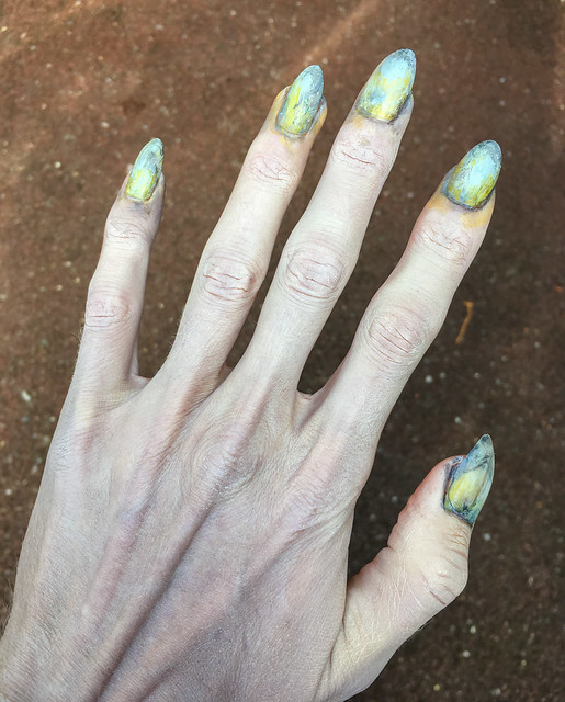 Photo of one of my hands with pale makeup and long greenish nails