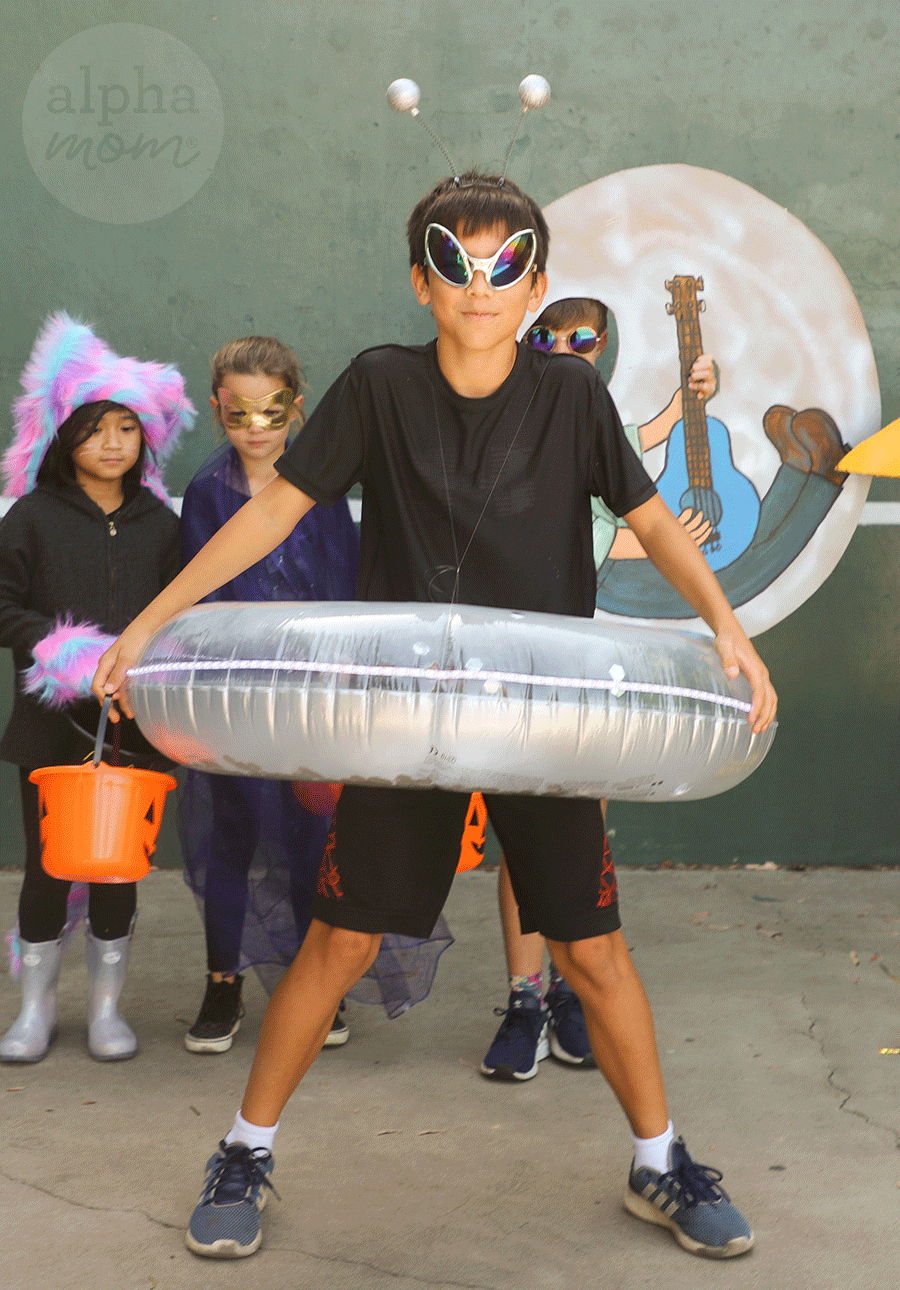 kid wearing DIY Space Alien costume of silver inner tube with bug-eyed sunglasses and headband with silver balls on antennae and other kids in costumes in background