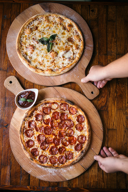 A waiter placing two pizzas on a wooden table at a restaurant