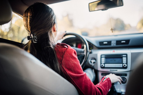 Woman in red shirt driving car, seen from perspective of rear seat passenger