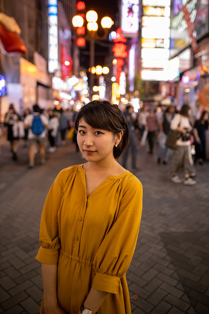 Portrait of young woman standing in the middle of busy shopping street at night