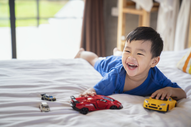 Asian boy fun and play a car toy on the bed