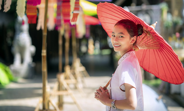 Asian girl in northern traditional costume and red umbrella stand in temple