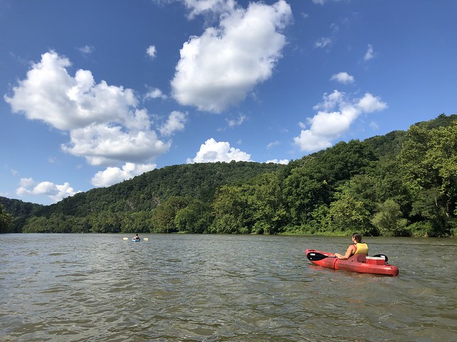 Two kayakers paddling in the New River beneath a blue sky with white clouds.