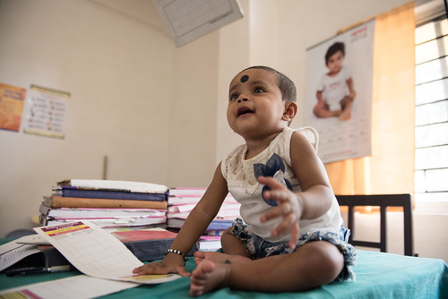 Eleven-month-old Muskaan Doom smiles while sitting on a table in the Immunization Room at Assam Medical College, Dibrugarh. Her mother, Raj Nandini, is an employee at AMC. | by International Vaccine Access Center