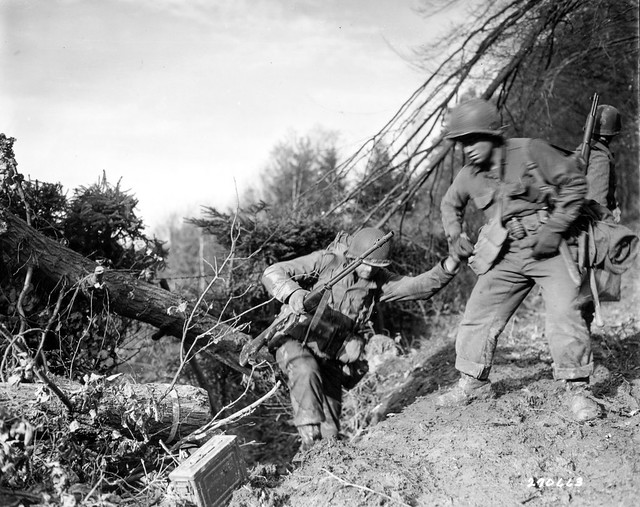 SC 270663 - Pfc. Benny Barron of St. Louis, Missouri gives a helping hand to a buddy as they make a difficult climb in the Hurtgen Forest, southwest of Duren, Germany, during the Allied offensive. 18 November, 1944.