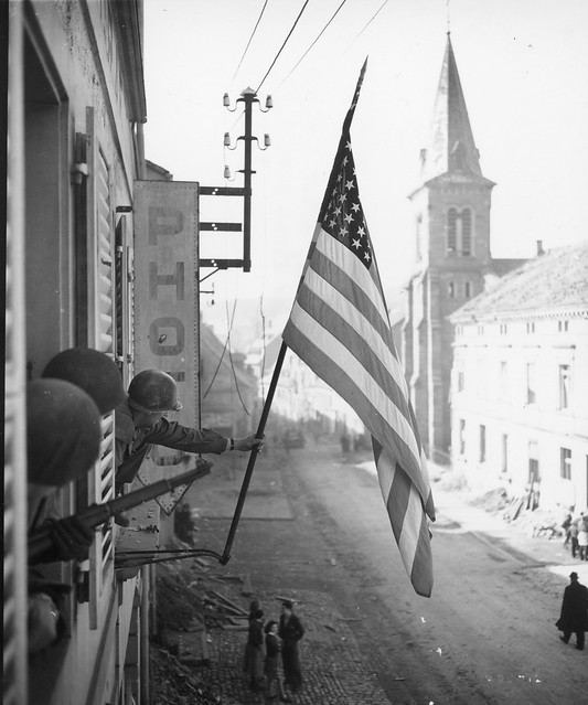 SC 202712 - Capt. Thomas H. Garahan, Brooklyn, New York, raises American flag as Bitche, France, falls to the 100th Infantry Division, US Seventh Army, after a siege of many months. He was with the first troops to enter the town. 16 March, 1945.