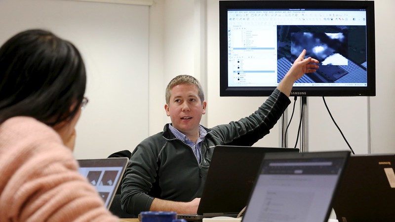 Two people discussing a research question at a desk in front of a large screen 