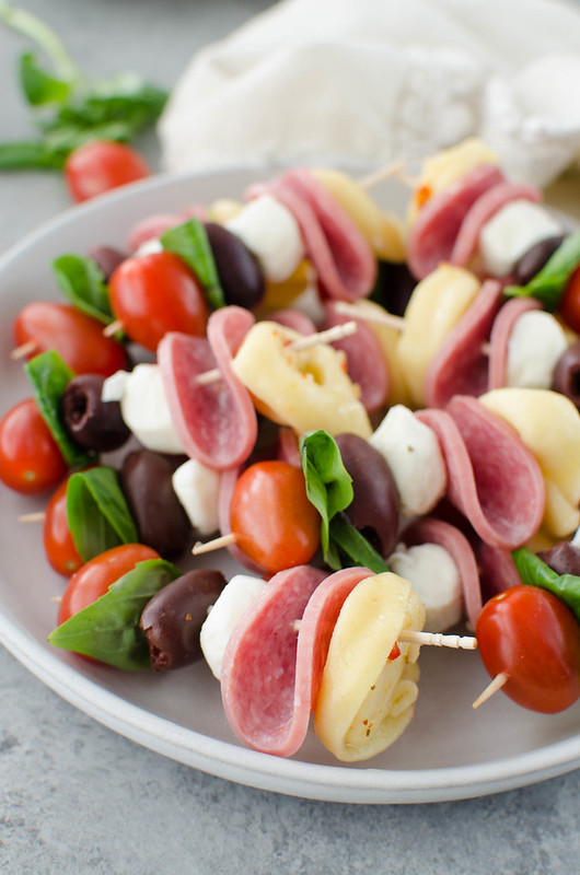 Antipasto Skewers - the easiest party appetizer! Cheese tortellini, Genoa salami, mozzarella balls, fresh basil, olives, and grape tomatoes layered on skewers. 