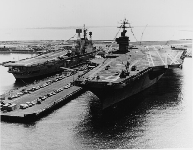 USS NIMITZ (CVN-68) and HMS ARK ROYAL (R09)) Berthed at the Norfolk Naval Base, Virginia, in April 1976. They are dressed with flags in honor of the birthday of Queen Juliana of the Netherlands