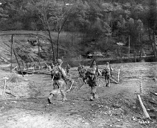 SC 196622 - Deep in the Hurtgen forest, in Germany, American infantrymen move across a bridge over a small stream. A tank, part of the new Allied offensive, can be seen in the background. 18 November, 1944.