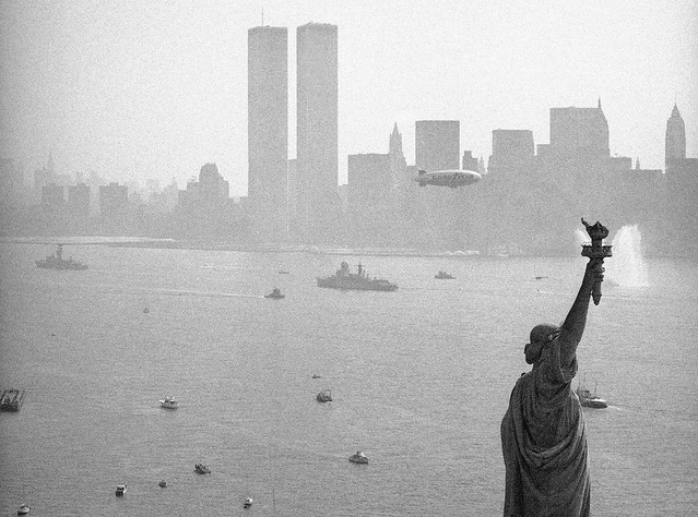 The Statue of Liberty, a Good Year blimp and warships plying the waters of the Hudson River pass by the World Trade Center and the smoggy New York skyline. Operation Sail on America's Bicentennial day. New York. July 4 1976.