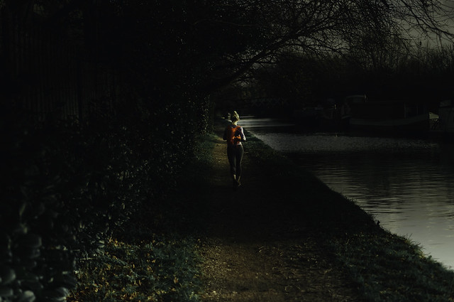 lady runner with red backpack running down canal towpath