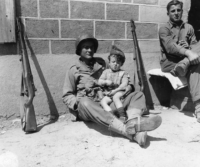 SC 190646 - Pvt. William L. Hatcher, of Scranton, SC, amuses a little French orphan by letting him wear his garrison cap. 20 June, 1944.