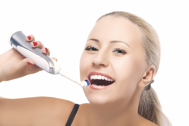 Concept of Dental Health: Blond Caucasian Woman Brushing Her Teeth with Electric Toothbrush