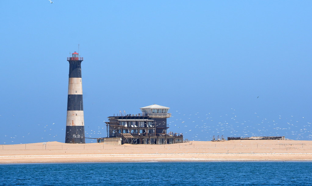 A LIGHTHOUSE SURROUNDED BY A LONG SKINNY SPIT OF SAND.  IT WAS ORIGINALLY BUILT ON THE END OF THE SPIT BUT SINCE THEN, THE SAND HAS CREATED A VERY LONG PENINSULA.  THIS LIGHTHOUSE IS IN NOW THE MIDDLE.  WALVIS BAY,  NAMIBIA