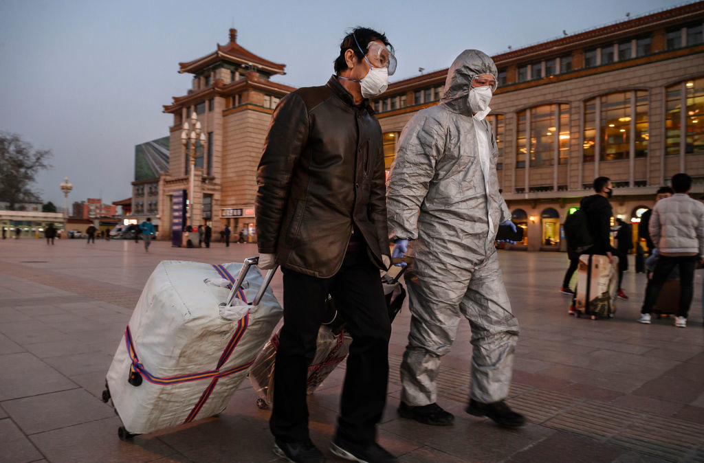 旅客身著口罩與防護衣前往北京車站搭車。（圖片來源：Kevin Frayer / Getty Images）