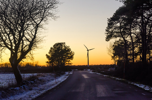 Vinterväg med vindkraftverk i solnedgången