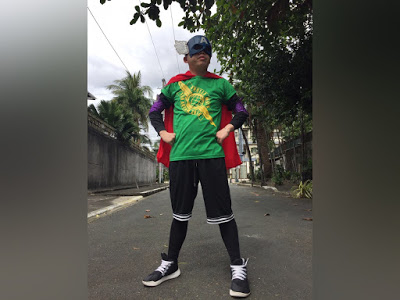 The image shows PWA Gio Koe wearing 2018 Angels Walk t-shirt, winged mask, superman like costume, and black and white pants and shoes.