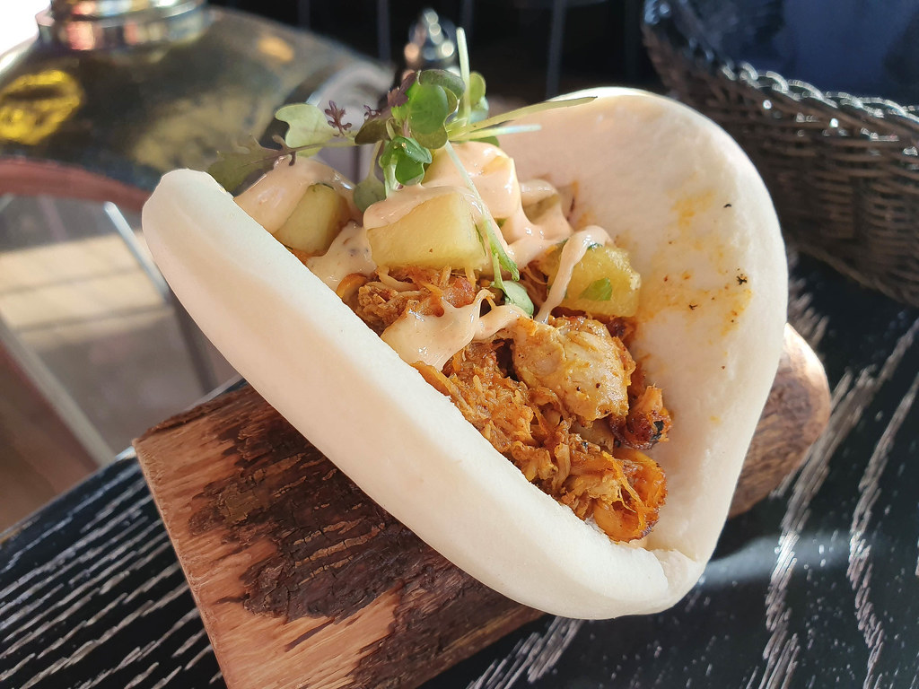 Picture of a white bao bun filled with slow roasted pork, pieces of yellow pineapple and white Japanese mayo on top