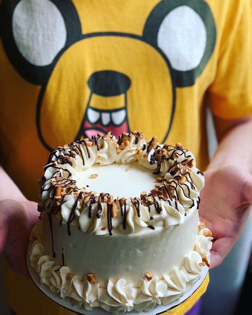Man wearing t-shirt of Adventure Time's Jake th4e Dog character while holding a beautifully frosted cake