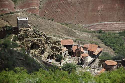 horizontal outdoors people priest walking maninblack spire church building architecture tower stone cross religion belief hills rock mountain colorful minerals sandstone volcanic rainbowhills hill landscape dry depthoffield dof foregroundblur plant green bush roof rooftile rockhewn cavesinrock summer travelling travel colour color june 2018 vacation canon camera photography canon5dmkii kakheti davidgareja monastery georgia eurasia easterneurope westasia monasterycomplex