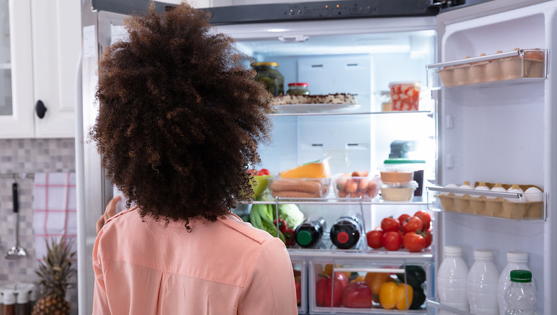 A woman looking into an open fridge full of food and drinks.