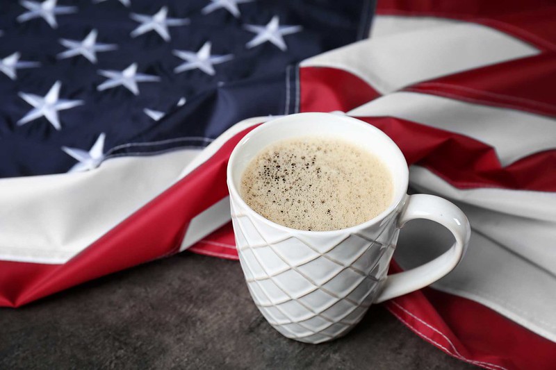 Cup of coffee and American flag on grey background