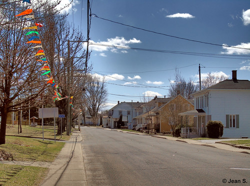 village rural street sky clouds flags grass blue white green sidewalk empty house