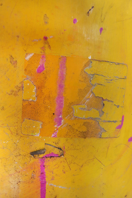 abstract of ripped-off tape and dripped pink on a yellow bollard