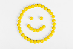 Smiley face from yellow pills on white background, top view