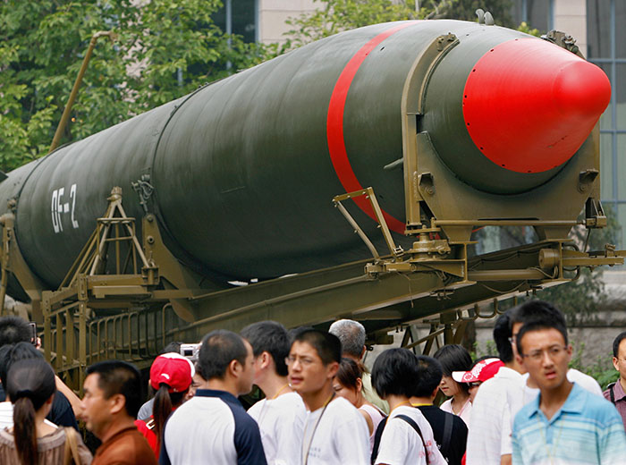 People walk past a missile on display outside of a museum.