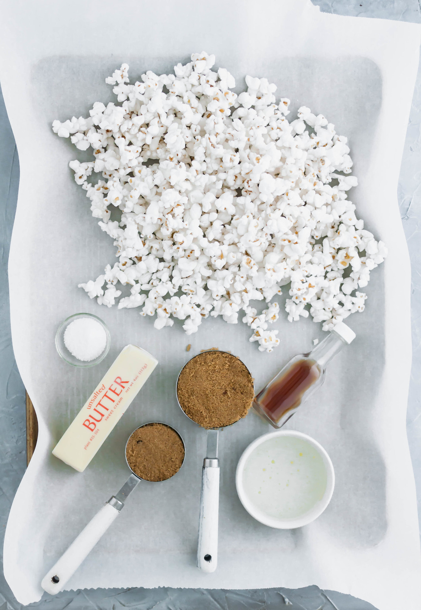 Ingredients needed for salted caramel corn on a baking sheet lined with parchment paper.