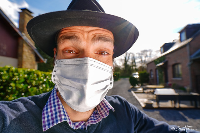 Man wearing a protective face mask, blue gloves and coveralls against the Coronavirus Covid-19 SARS-CoV-2 at home during lockdown and quarantine - Ben Heine Photography