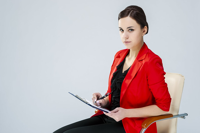 Portrait of Positive Confident Female Enterpreneur Posing in Red Blazer And Notepad While Making Notes Against White