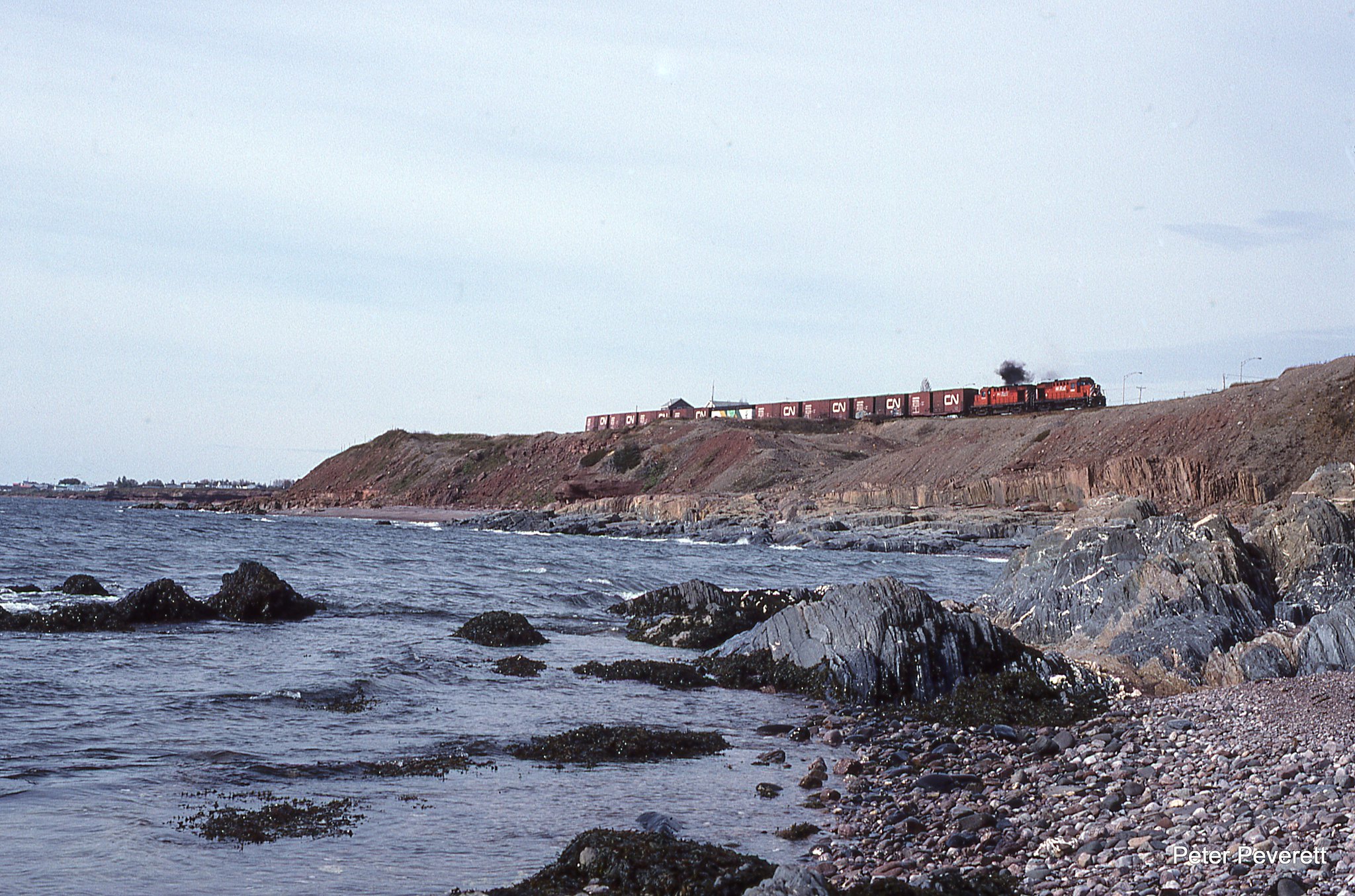 NBEC RS-18 # 1868, 1840 on Train 592 is seen on the edge of Chaleur Bay at 1105 AM Oct. 4, 2000 at St.Therese-de-Gaspe, Quebec. In 1950 mining started in the town of Murdochville. Raw ore finished with a end product of pure copper anode. By 1999 the mine closed and the last of the copper was being loaded into CN box cars in Gaspe.  The Town of Murdochville went from a population of 5,000 in the 1970s to 764 people by 2011.  One of only a couple of inland towns on the Gaspe peninsula and several miles from anything the town has had to fight to survive.   