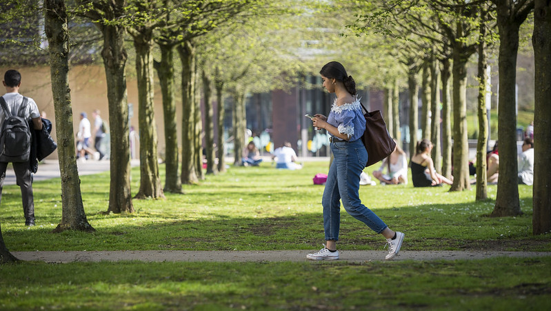 Girl walking under trees looking at her phone