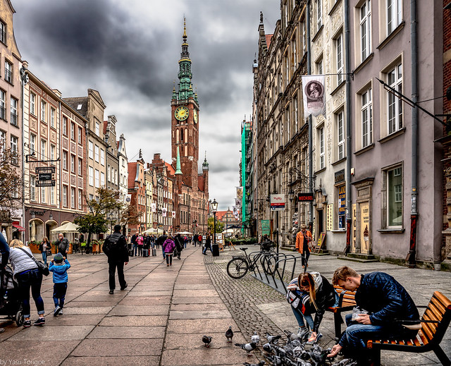 A couple taking time to feed pigeons on the Royal Route view of the Main Town Hall, Gdansk, Poland.  622-Edita