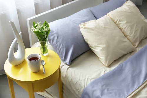 Unmade bed with crumpled blue bed linens and side table | by PhilStephenson