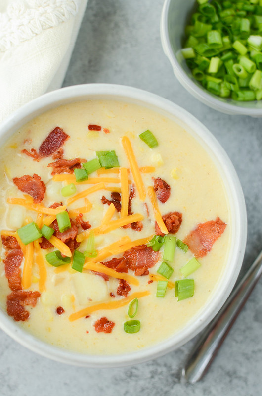 Corn chowder topped with cheddar cheese, bacon, and green onions in a white bowl