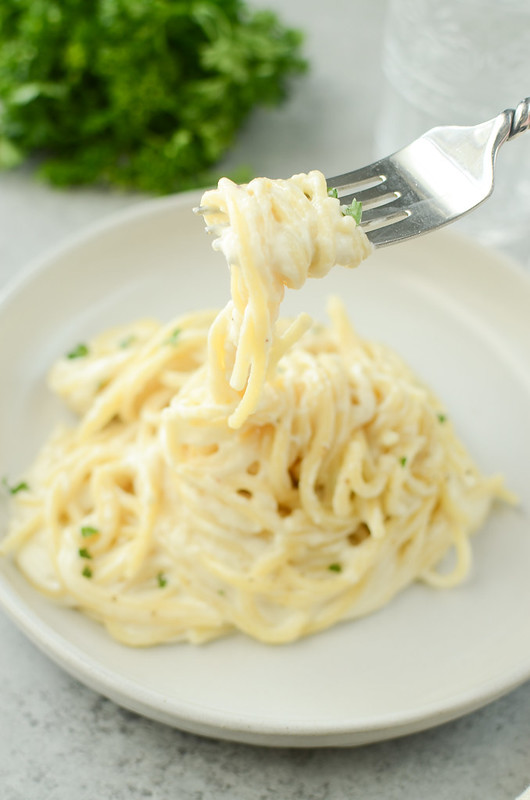Creamy cheesy spaghetti on white plate; fork lifting spaghetti off plate
