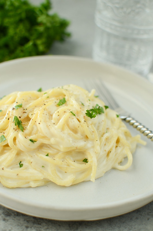 Cheesy spaghetti on a white plate with parsley and black pepper on top
