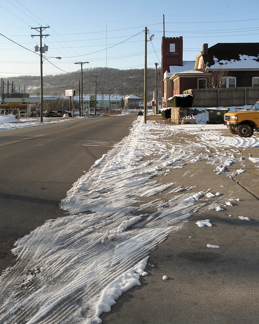 An Appalachian sidewalk is covered in icy tire tracks.