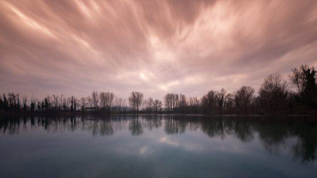 A red and cloudy sky reflected in the water of a lake at sunset time