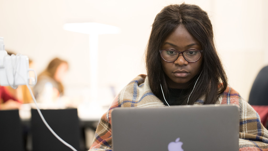 female black student wearing glasses and headphones sat in front of a laptop