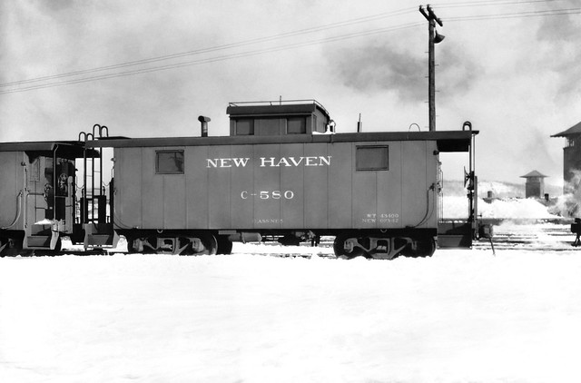 New Haven Railroad NE-5 class welded steel caboose # C-580, is seen spotted on the caboose track in the yard while in the snow at Maybrook, New York, ca winter mid 1940's