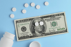 Pharmaceutical pills, hundred dollar bill and bottle on blue bac